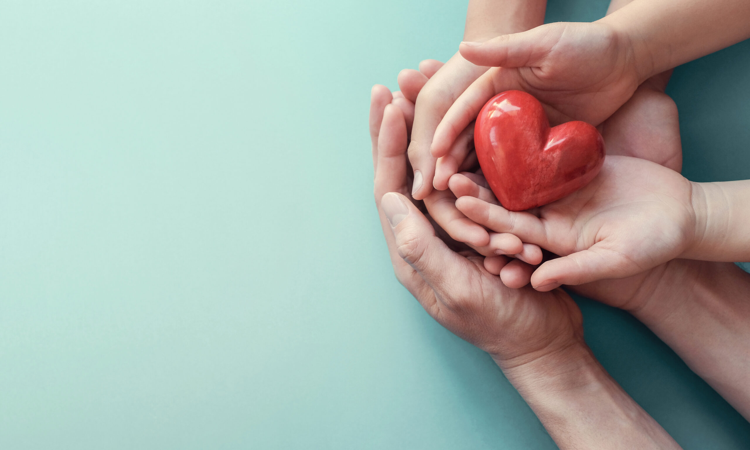 Adult and child holding a red heart together, symbolizing family heart health, prevention, and healthy lifestyle habits.