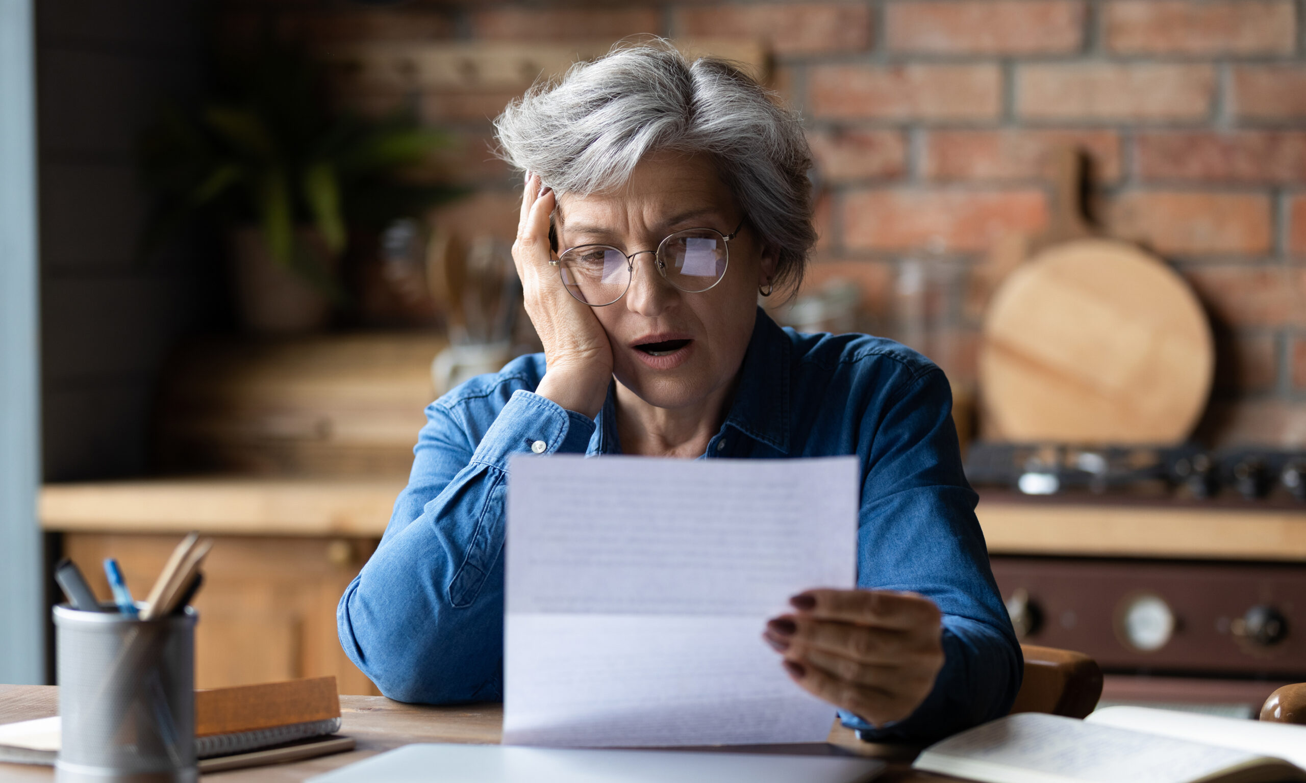 Older woman reading an official letter at her kitchen table with a worried expression, symbolizing loss of Medi-Cal coverage and exploring available options.