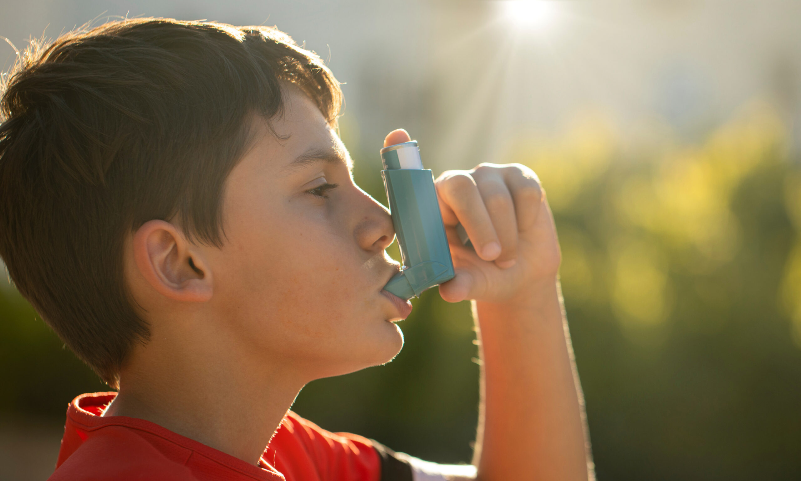 Child using an inhaler outdoors, highlighting the importance of asthma management and back-to-school health checkups for kids.