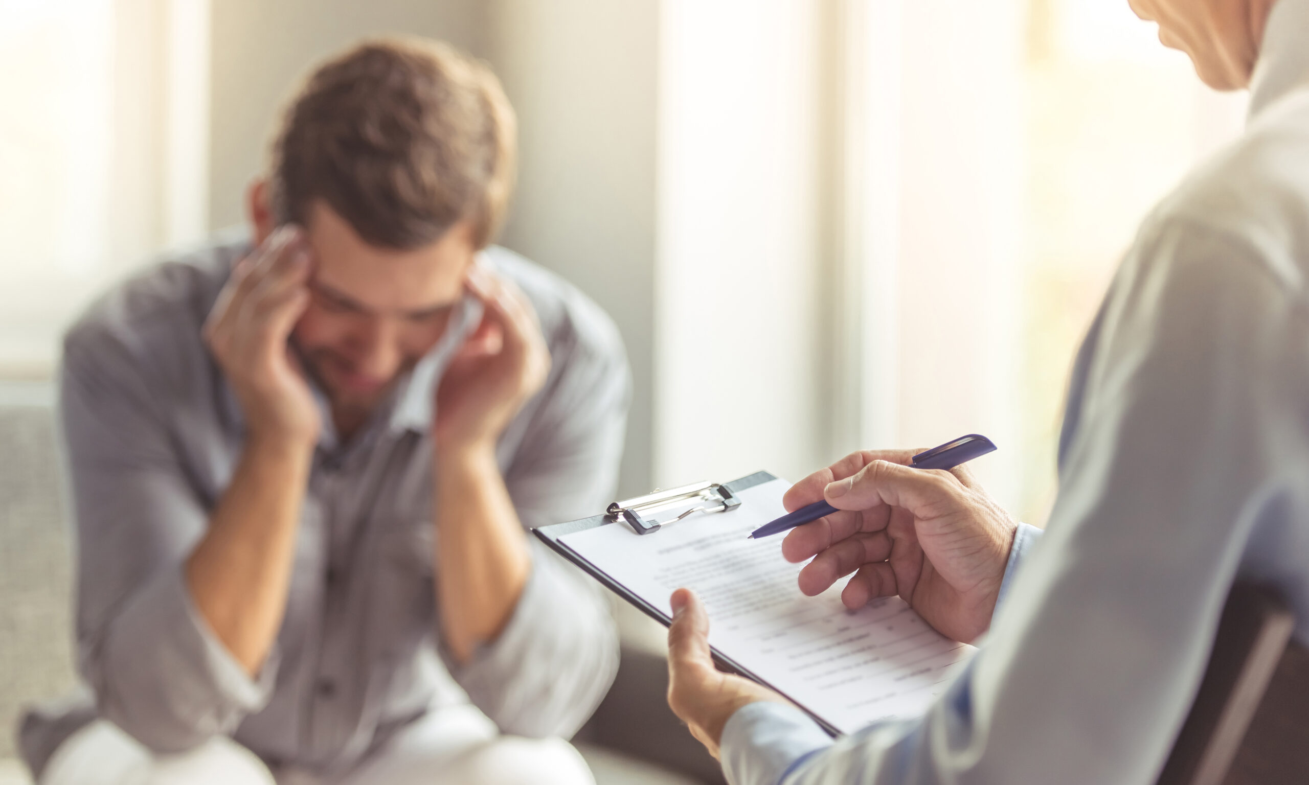 psychiatrist taking notes while patient is visibly stressed and dealing with mental anguish