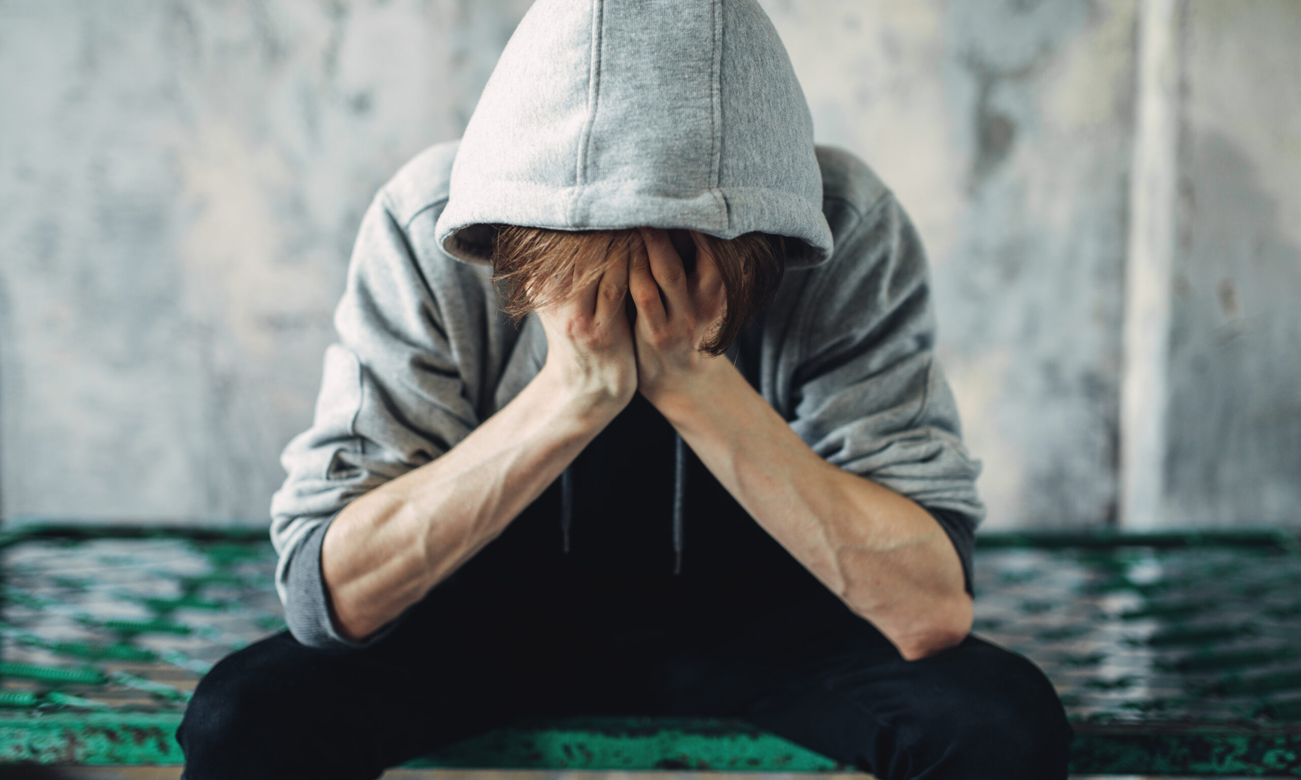patient wearing hoodie covering face with hands in anguish feeling heavy weight of addiction